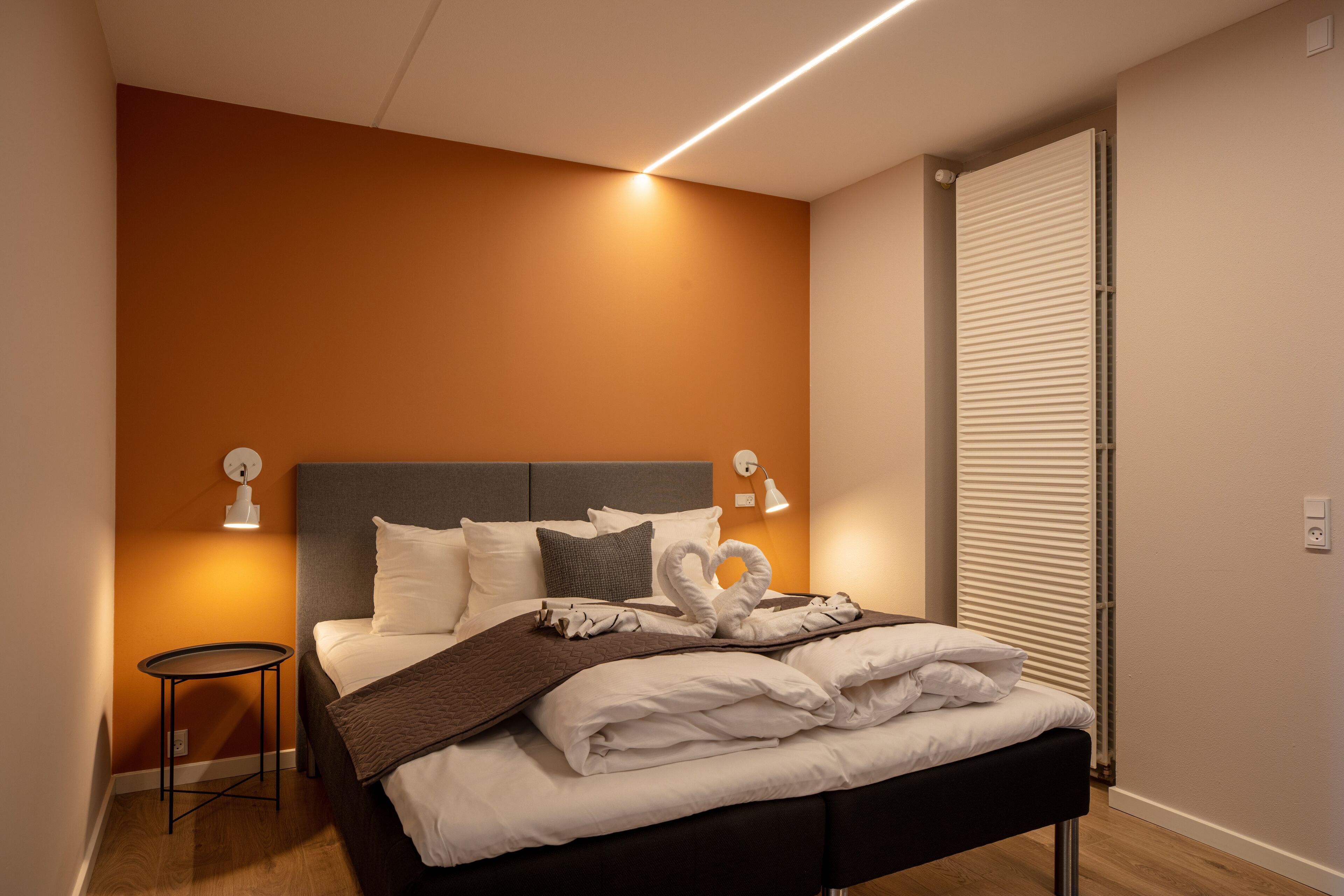 Una camera d'albergo moderna con un letto rifatto, un tavolino e un termosifone.