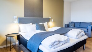 Una habitación de hotel moderna con una cama grande, una mesita auxiliar pequeña, un sofá y una lámpara de pared.