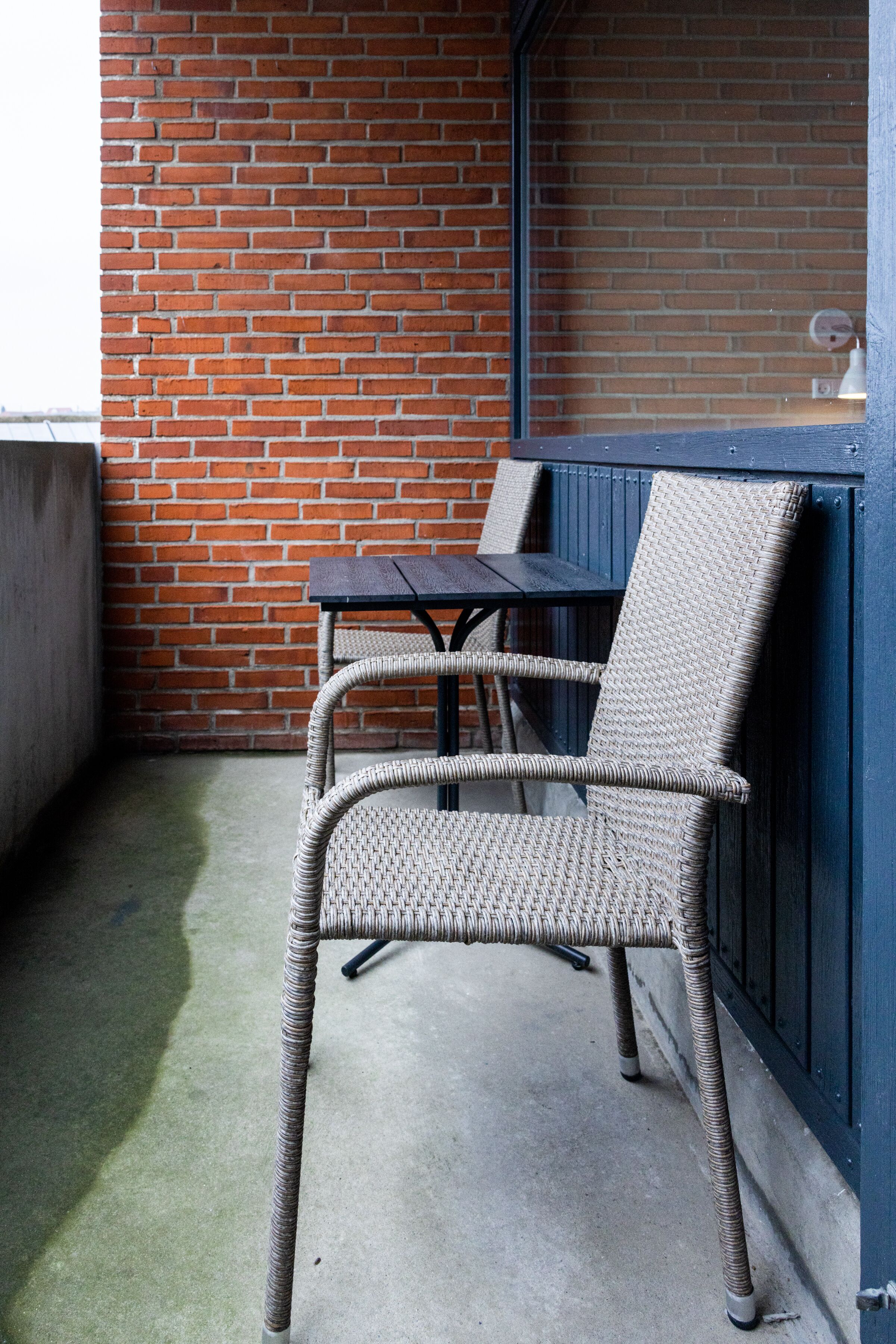 A wicker chair and table set against a brick wall and blue paneling.