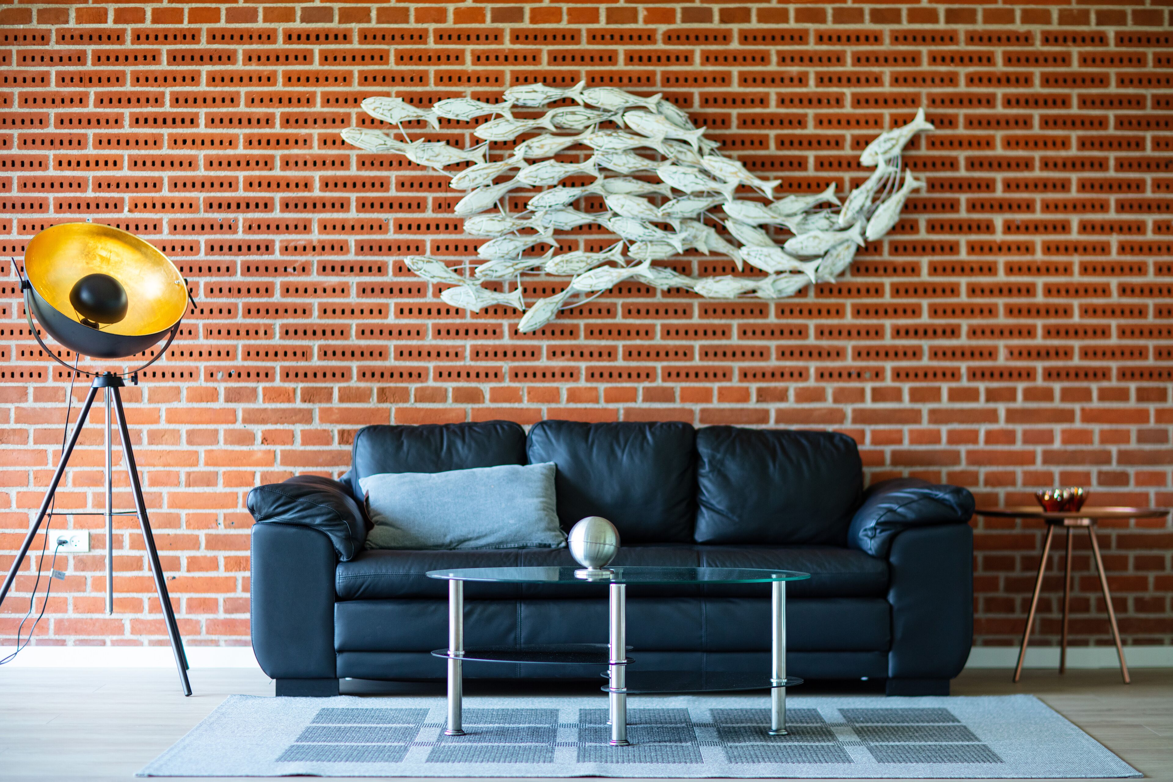 Un saló modern amb una paret de maó, un sofà de pell negra, una taula de centre de vidre i una obra d'art mural decorativa amb motius de peixos.