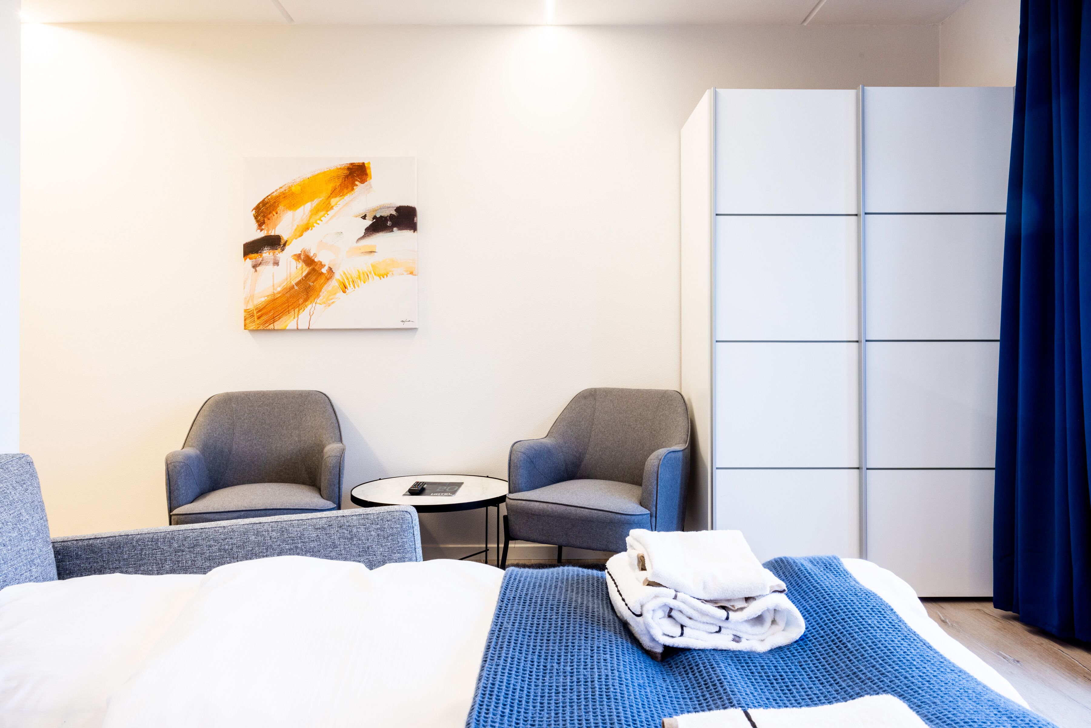 Habitació d'hotel amb un llit, dues butaques, una taula petita, un quadre a la paret i un armari.