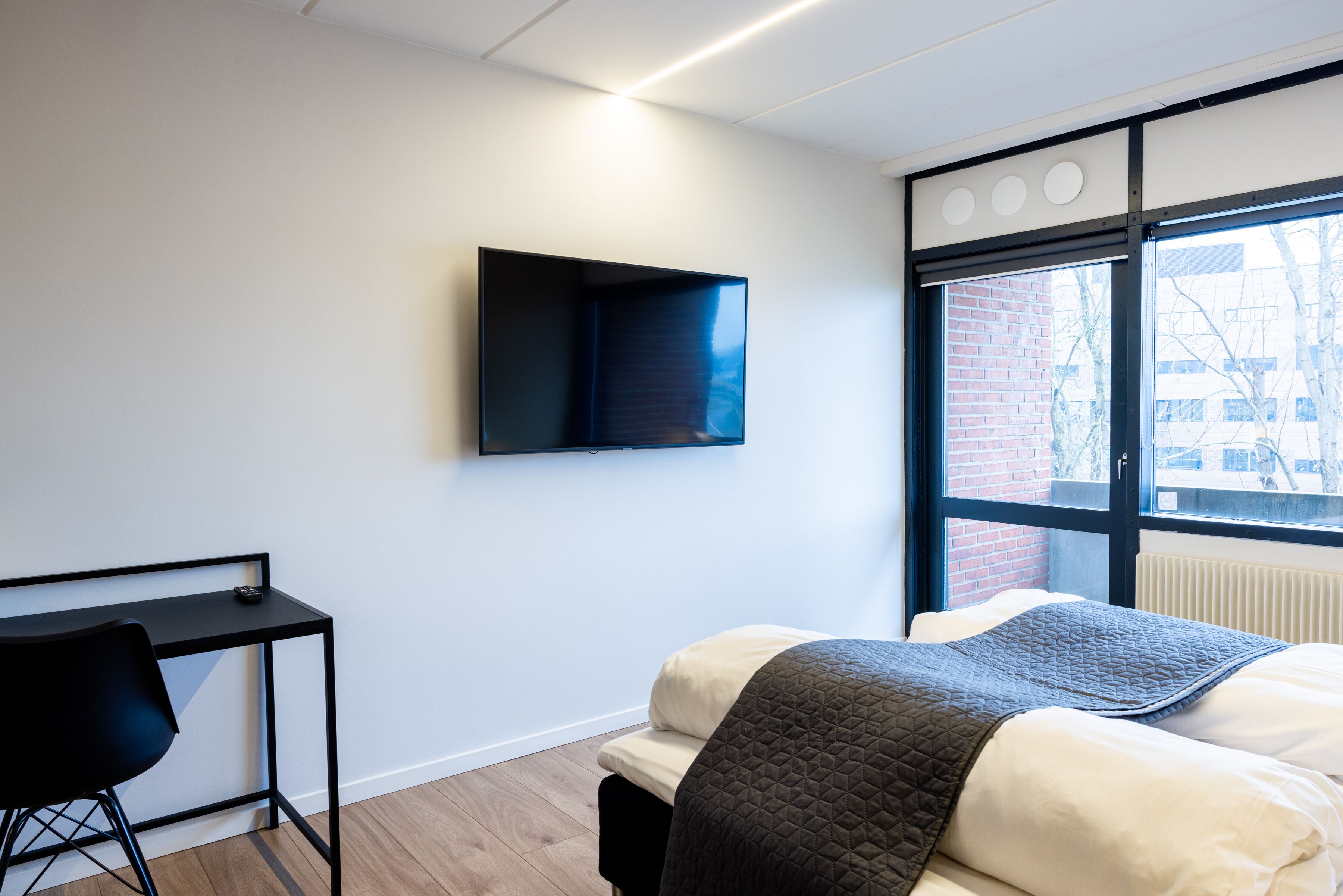 Una habitación de hotel moderna con cama, escritorio y televisor montado en la pared.