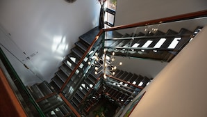Un espacio interior de varios niveles con barandillas de vidrio, una escalera central y una lámpara colgante.