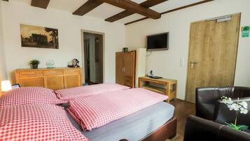 A bedroom with two beds, a wooden wardrobe, a television, and a door with a sign.