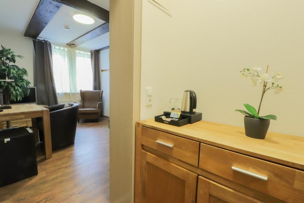 A room with a wooden desk, a chair, a potted plant, and a small table with a kettle.