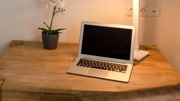 Een houten bureau met een laptop, een potorkidee en een bureaulamp.