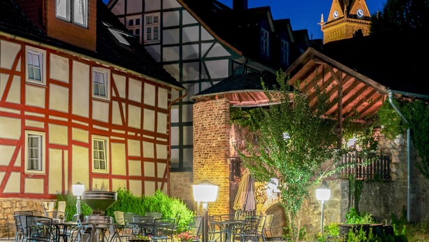 Een traditioneel Europees gebouw met zichtbare vakwerkconstructie, een stenen toren en een buitenterras met tafels en stoelen.