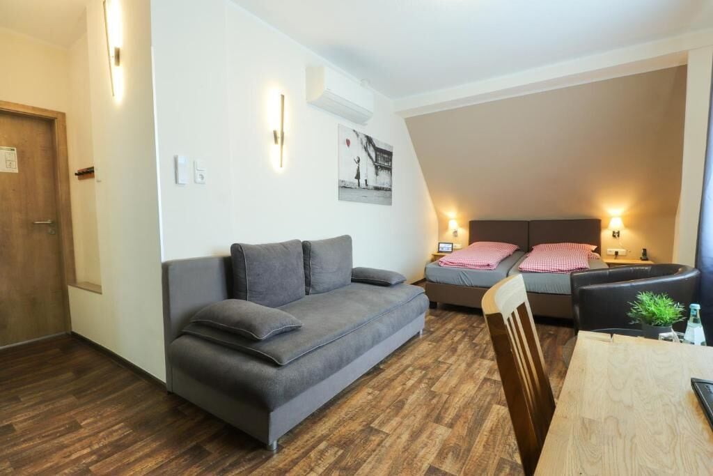 A compact living space with a sofa, a bed with pillows, a bedside table, and a small table with a chair.