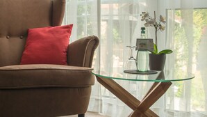 Een bruine bank met een rood kussen, een glazen salontafel met houten poten, en een orchidee in een pot op de tafel.