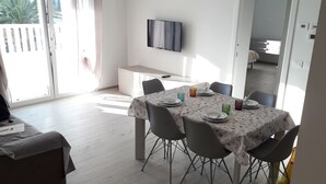 A dining area with a table set for four, a TV mounted on the wall, and a view of the outside through a sliding door.