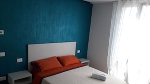 A bedroom with a bed, orange pillows, white headboard, and a window with curtains.