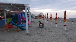 A beach with a playground, beach umbrellas, and a sandy area.