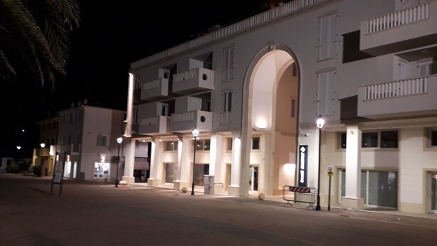 A multi-story hotel with balconies, a central archway, and a street in front.