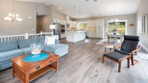 A spacious living area with a grey sofa, a wooden coffee table, and a black leather chair. A kitchen with white cabinets and a dining area with a table and chairs is visible in the background. - Beautiful newer home in Sudden Valley offering stunning lake view, golf and more (Bellingham)