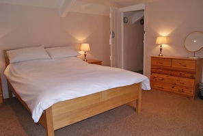 A bedroom with a wooden bed, two bedside tables with lamps, a wooden dresser, and a door leading to another room.