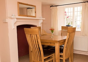 A dining room with a wooden table and chairs, a fireplace, a mirror, and a window with curtains.