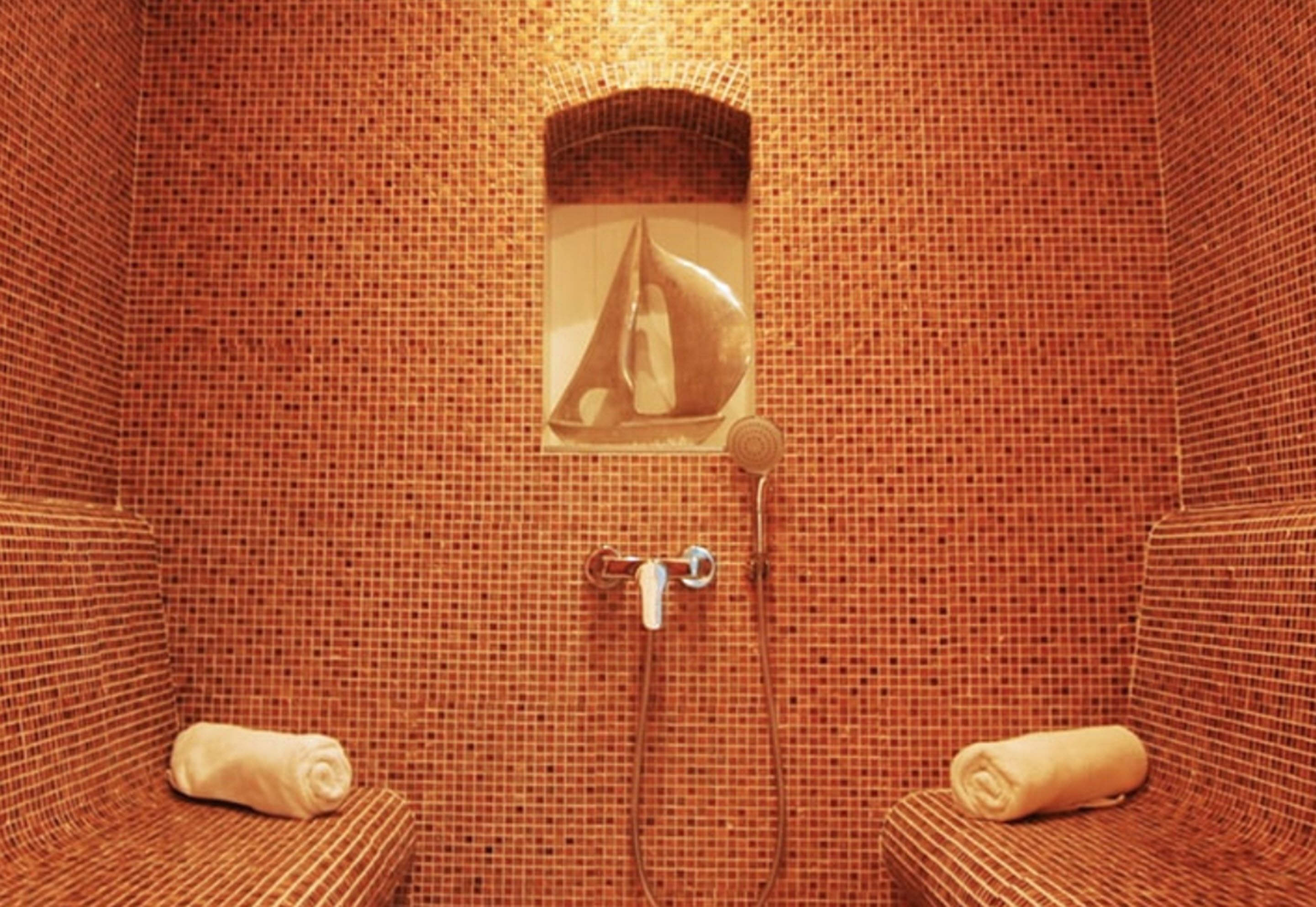 Une pièce avec un mur recouvert de mosaïques, un espace douche et deux serviettes posées sur des chaises.