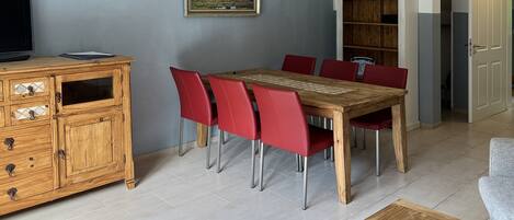 A dining area with a wooden table and red chairs, a wooden cabinet with drawers, and a painting on the wall.