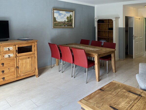 A dining area with a wooden table and red chairs, a wooden cabinet with drawers, and a painting on the wall.