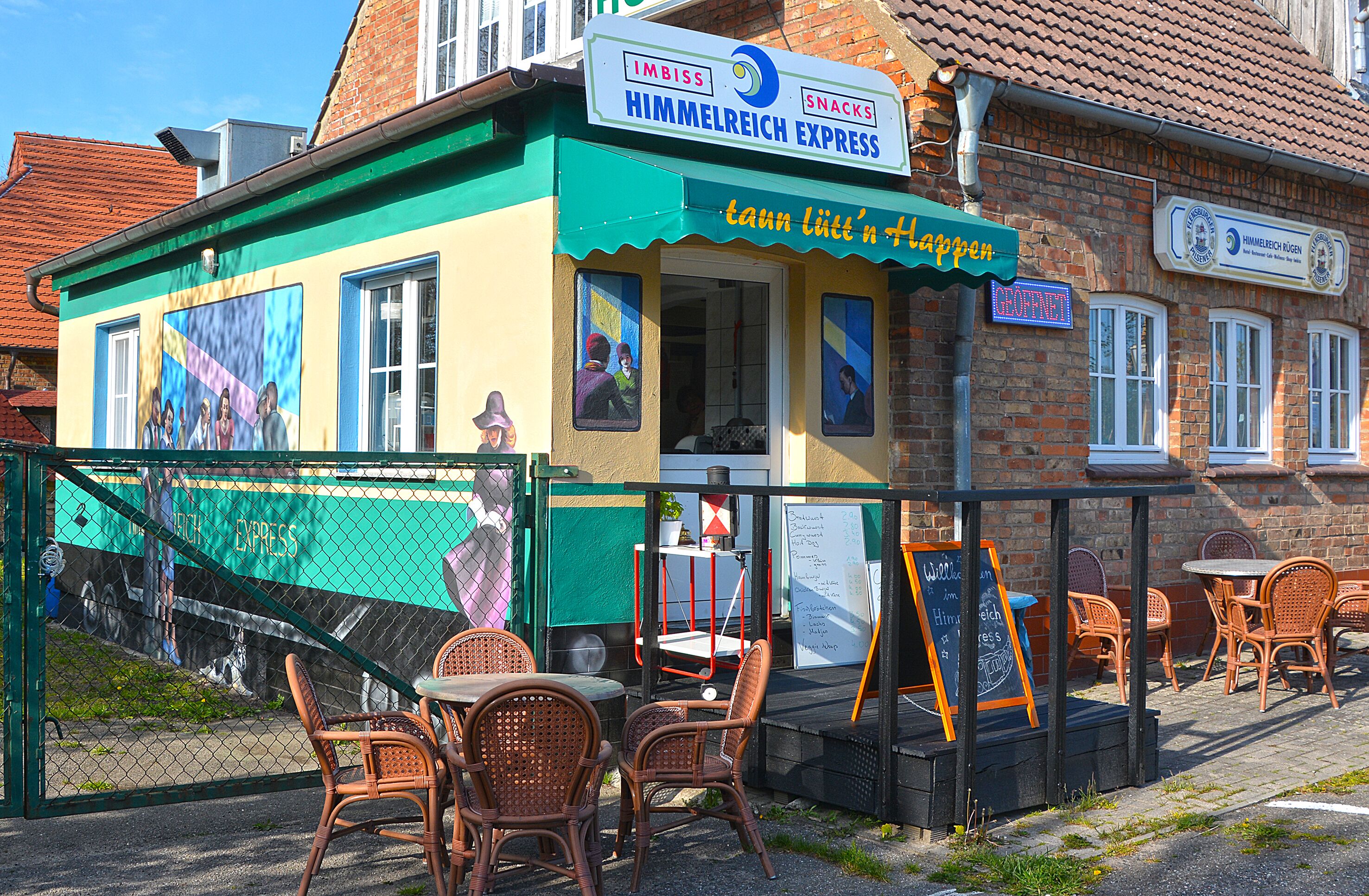 Ein Restaurant mit Außenbereich, Wandmalerei und Schild mit Werbung für Snacks und Lieferservice.