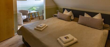 A bedroom with a large bed, two bedside tables, a chair, and a small table with a plant.