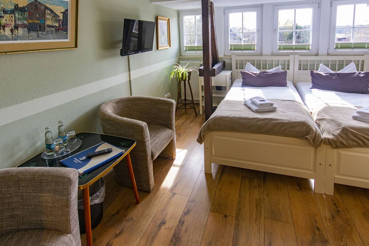 A hotel room with a bed, a chair, a small table with a tray, a TV, and a window with blinds.