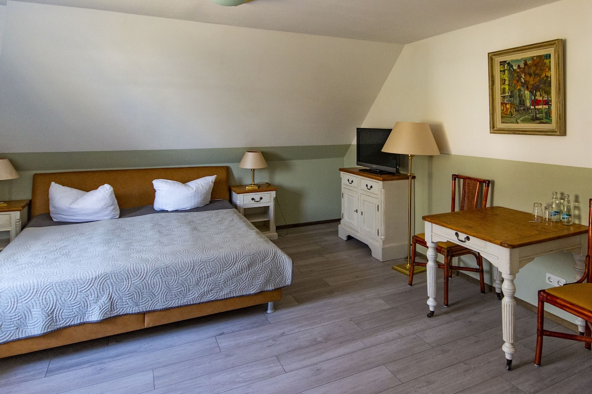 A hotel room with a bed, bedside tables, a desk, a chair, a television, and a painting on the wall.