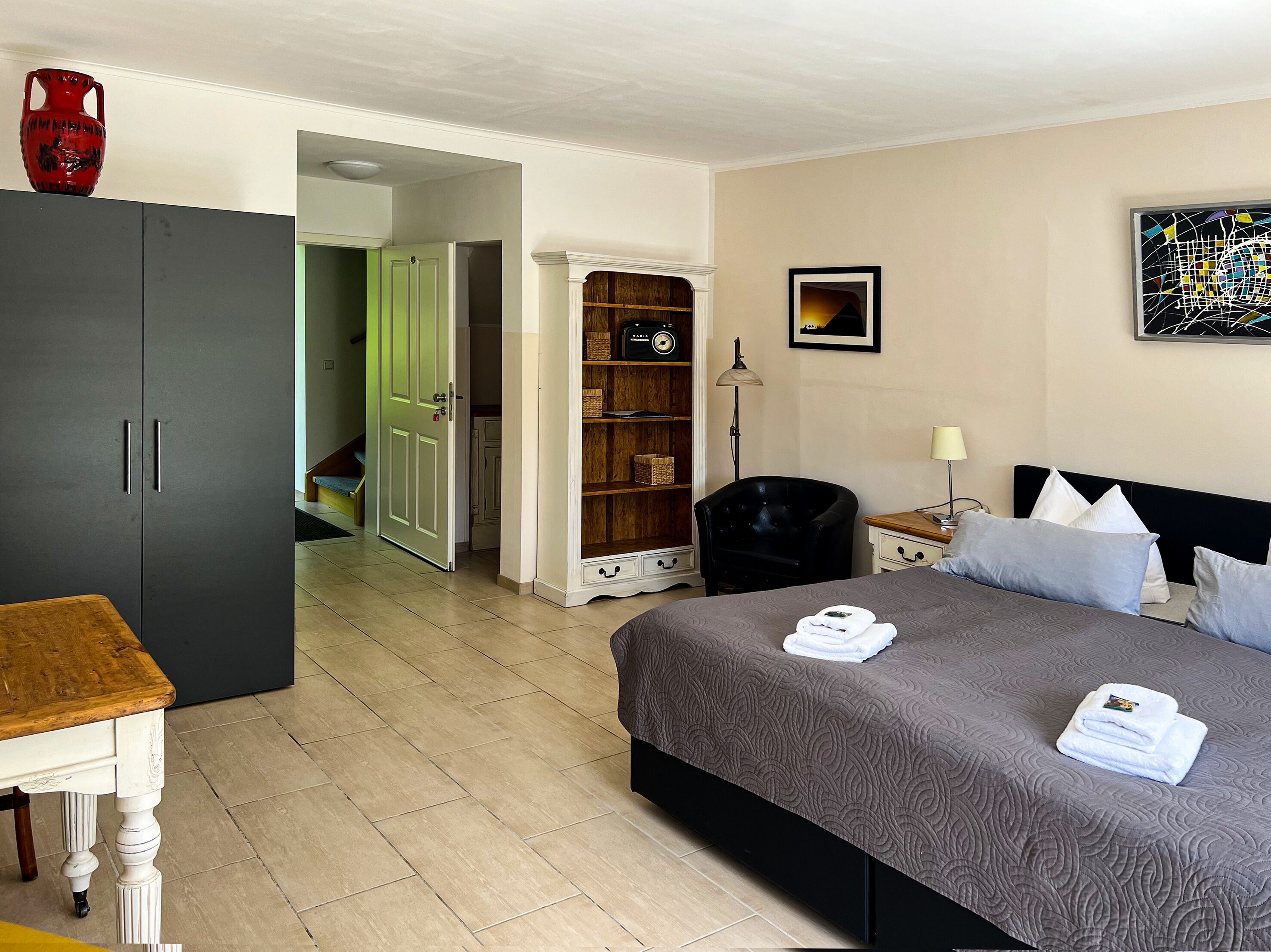 Et hotelværelse med en seng, et klædeskab, et skrivebord og en reol.