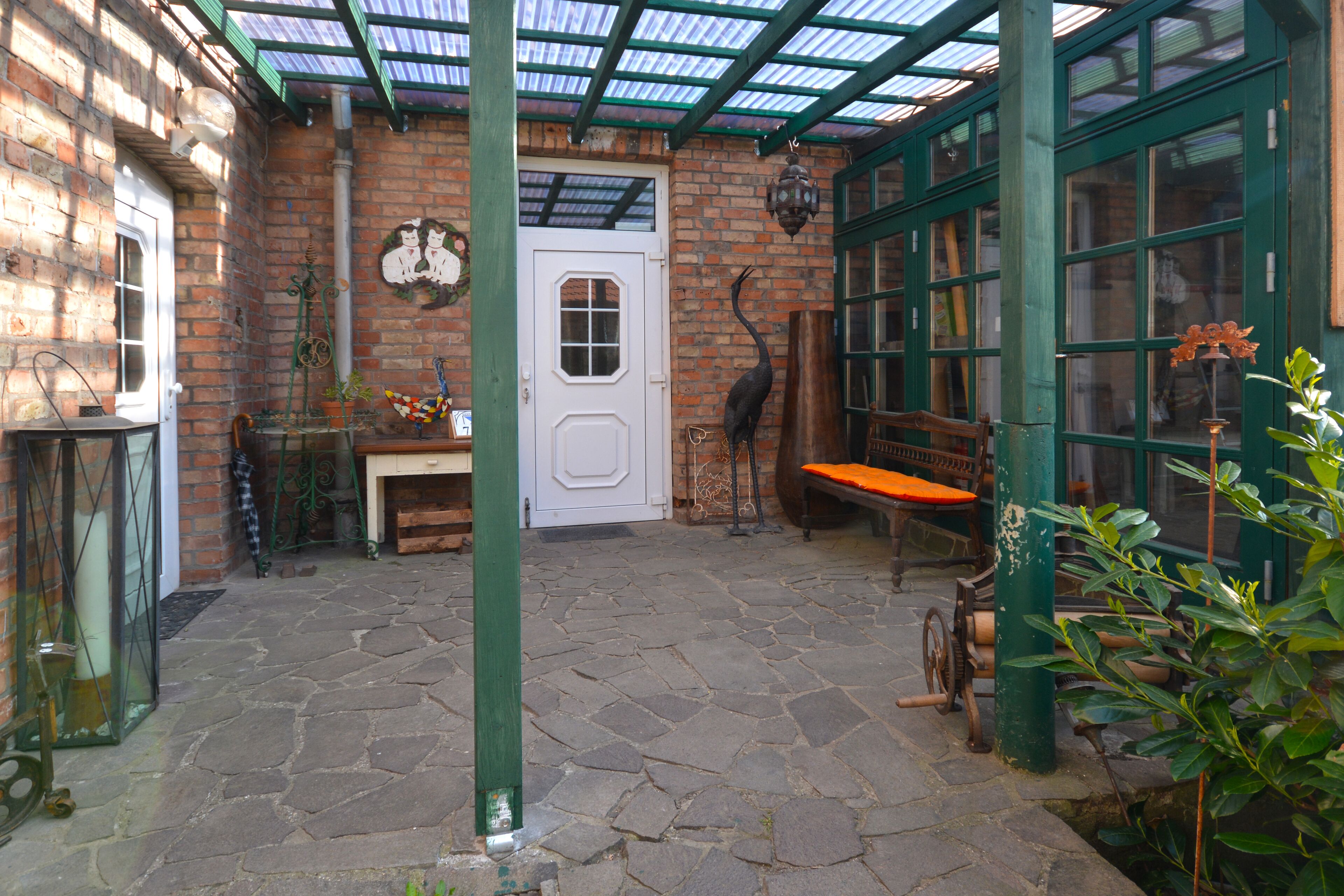 A covered patio with stone flooring, a white door, and a bench.