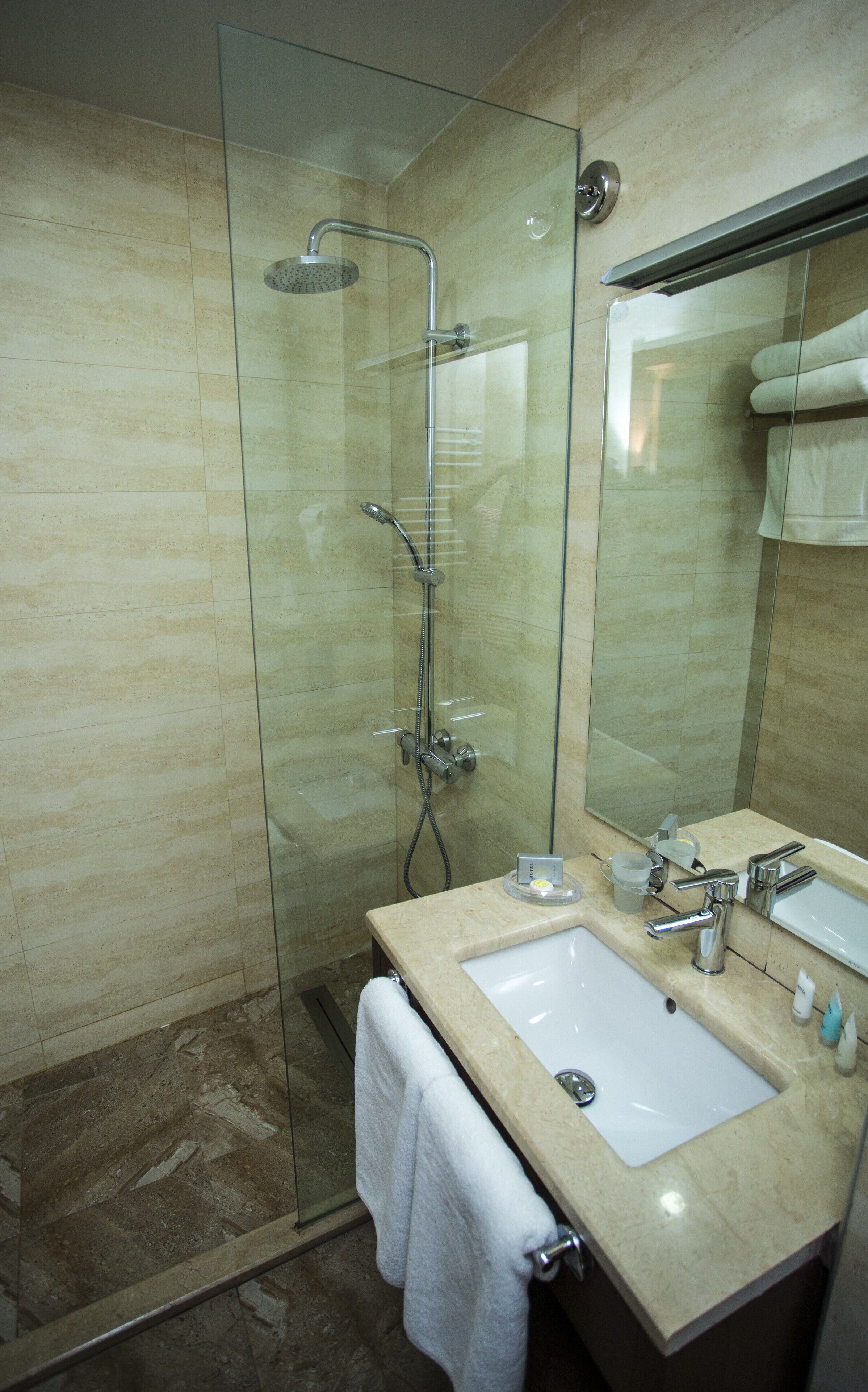 A modern bathroom with a glass-enclosed shower, a sink with a mirror, and a towel hanging on the wall.