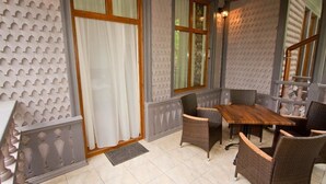 Une pièce d’angle avec une table en bois et des chaises en osier, une fenêtre avec des rideaux et un mur orné d’un motif.