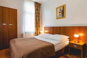 A bedroom with a bed, wooden wardrobe, a nightstand with a lamp, a window with curtains, and a painting on the wall.