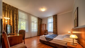 Une chambre d’hôtel avec un plancher en bois, un lit avec du linge de maison blanc, un bureau avec une chaise, une armoire et un téléviseur.