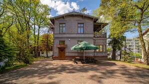 Un bâtiment à deux étages avec une façade en bois, un balcon et un parasol vert au-dessus d’une table de pique-nique.