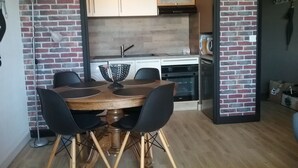 Ein Essbereich mit Holztisch und -stühlen, eine Küche mit Mikrowelle und Backofen sowie eine Uhr an der Wand.