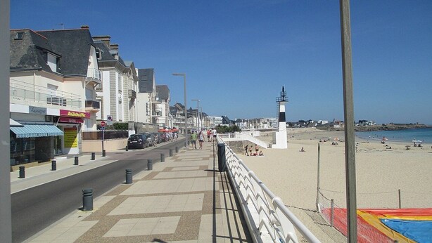 Eine Uferpromenade mit Geschäften, einem Strand und einem Leuchtturm.