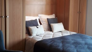 Ein Schlafzimmer mit einem Bett, zwei Stühlen, Holzschränken und einer Hängeleuchte.
