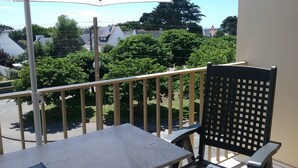Ein Balkon mit Tisch, Stuhl und Sonnenschirm, mit Blick auf Bäume und Häuser.