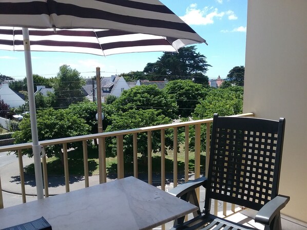 A balcony with a table and a chair, an umbrella, and a view of trees and houses. - Charming studio in Quiberon (Quiberon)