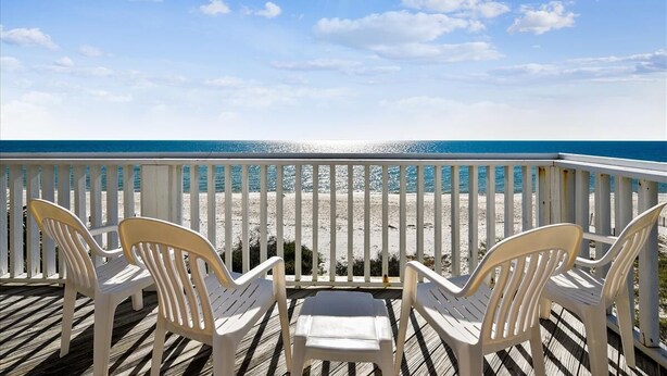 Een houten terras met witte plastic stoelen gericht op het strand.