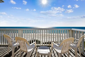 A wooden deck with white plastic chairs facing a beach.