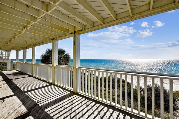 A covered wooden deck with a railing overlooking a beach.