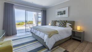 Un dormitorio con una cama grande, una mesita de noche, una lámpara, una silla y vistas al exterior.
