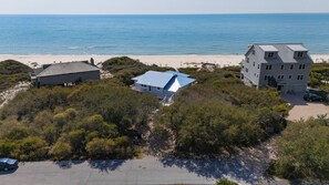 A beachfront property with multiple buildings, including a large house with a blue roof, surrounded by dense vegetation and a sandy beach.