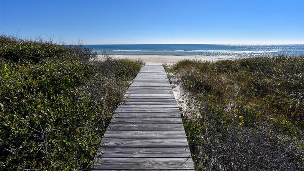 Un paseo marítimo de madera que conduce a una playa con cielos despejados.