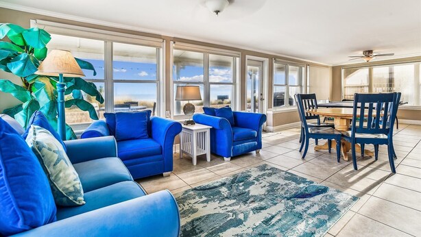 Un amplio salón con ventanas grandes, una mesa de comedor, muebles azules y un ventilador de techo.