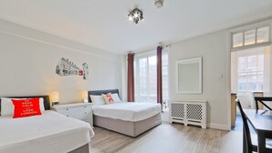 A hotel room with two beds, a dining table, and a large window with curtains. - Cosy Central Apartments - Oxford Street (London)