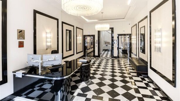 A hotel lobby with a check-in counter, black and white checkered floor, and a chandelier. - Cosy Central Apartments - Oxford Street (London)