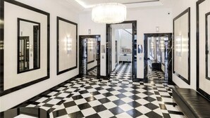 A hallway with black and white checkered flooring, framed mirrors on the walls, and a chandelier. - Cosy Central Apartments - Oxford Street (London)