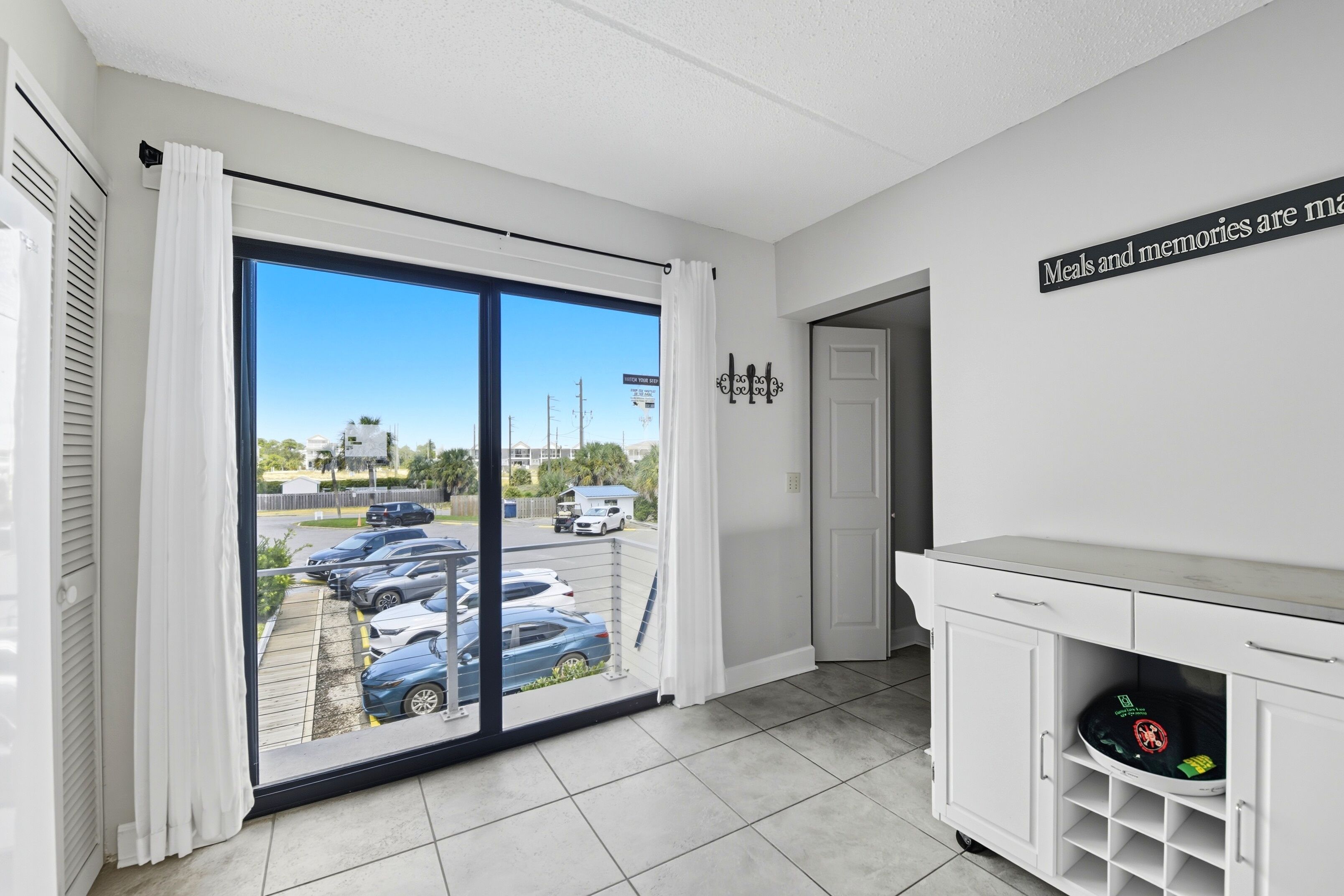 A room with a large sliding glass door leading to a parking area, a white cabinet with a shelf, and a wall-mounted sign.